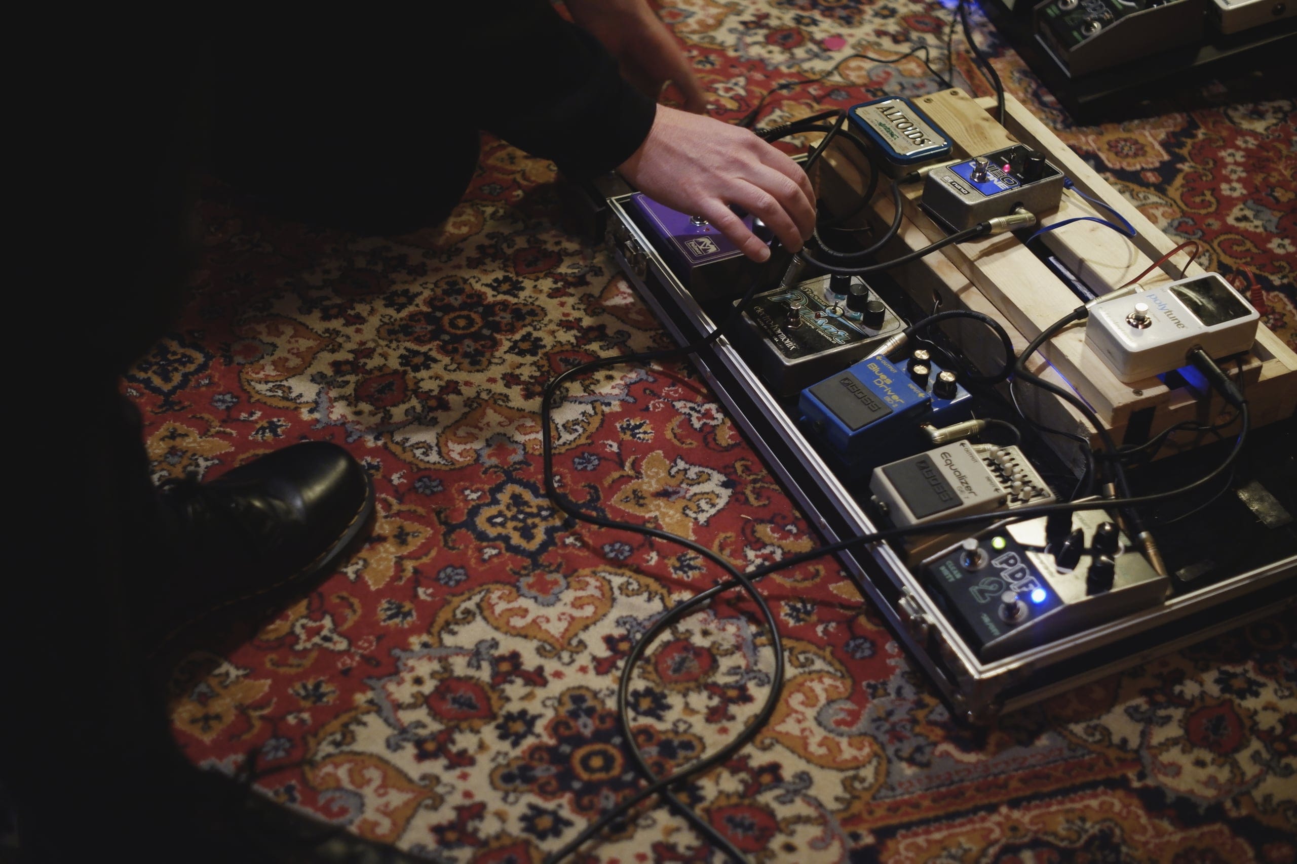 A musician adjusts guitar effects pedals on a patterned rug in the Andel Sound recording studio.